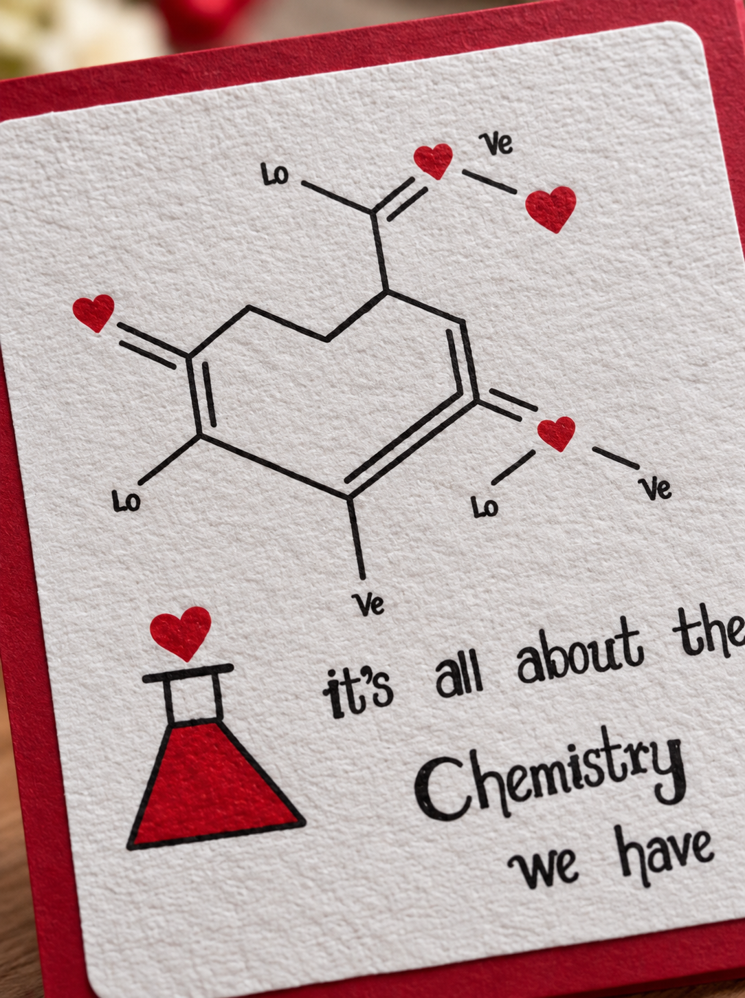 A close-up of a handmade greeting card featuring a chemical structure illustration with red hearts and the text 'it's all about the Chemistry we have', bordered by a red frame.
