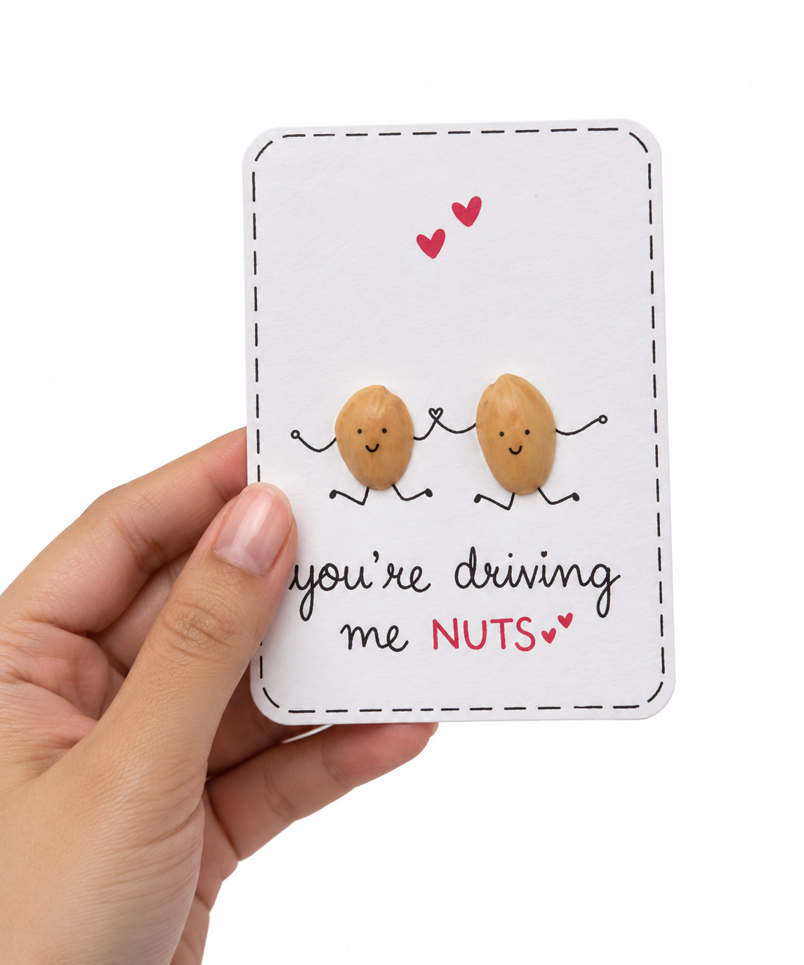 Handmade funny love greeting card held in a hand, featuring two cute peanut characters holding hands and the “You’re Driving Me Nuts” message.